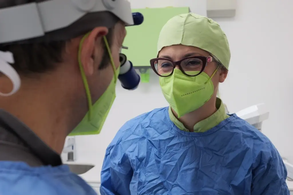 Il Dr. Scaringi e un membro del team medico dello studio dentistico con mascherina, cuffietta e dispositivi di protezione all'interno della clinica.